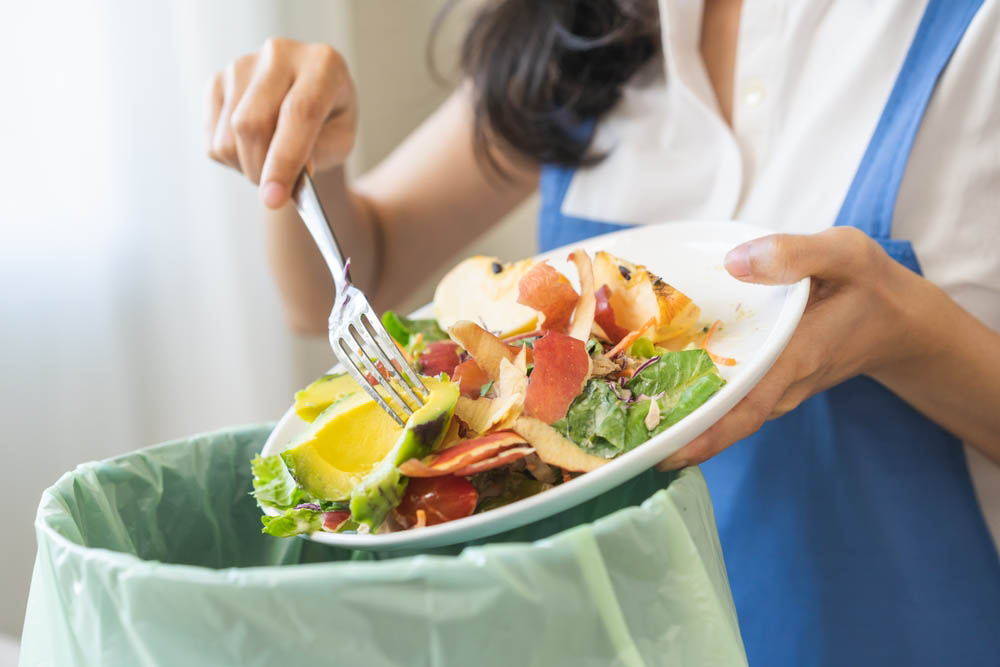 a person scraping food waste from a plate into the trash bin
